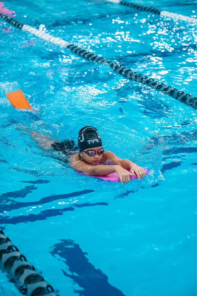 child using a kickboard and flippers in a swimming lesson